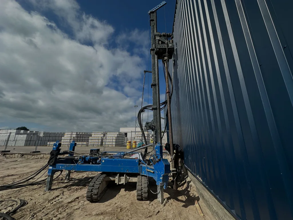 Boorstelling met hoge mast plaatst casing draaipalen direct langs de gevel van een bedrijfshal