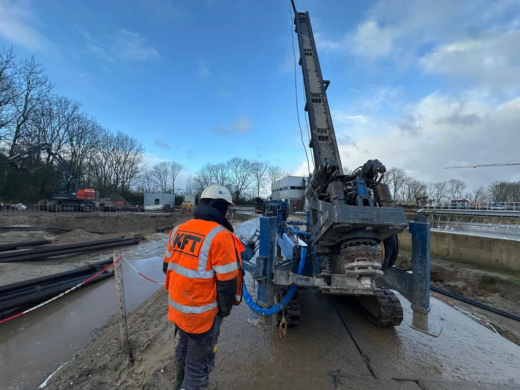 Medewerker in KFT-veiligheidshesje begeleidt een grote boorstelling voor casing draaipalen op een bouwterrein