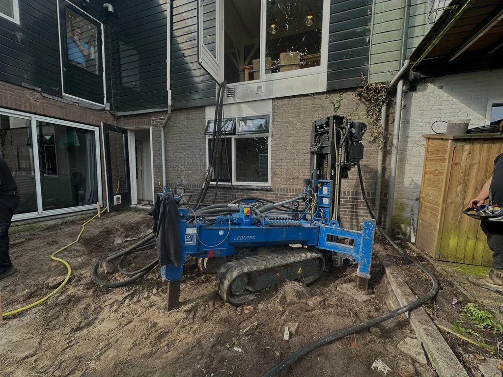 Compacte blauwe boormachine op rupsen boort schroefinjectiepalen in de achtertuin naast een woning