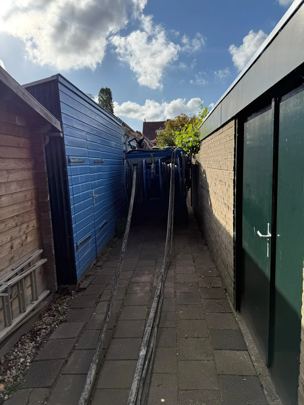 Slangen van de boorinstallatie lopen door een smal achterpad naar de werkplek voor de casing draaipalen in Breda