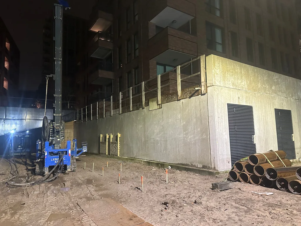 Boorstelling voor casing draaipalen in het donker naast een appartementengebouw in Nieuwegein, met gestapelde buizen