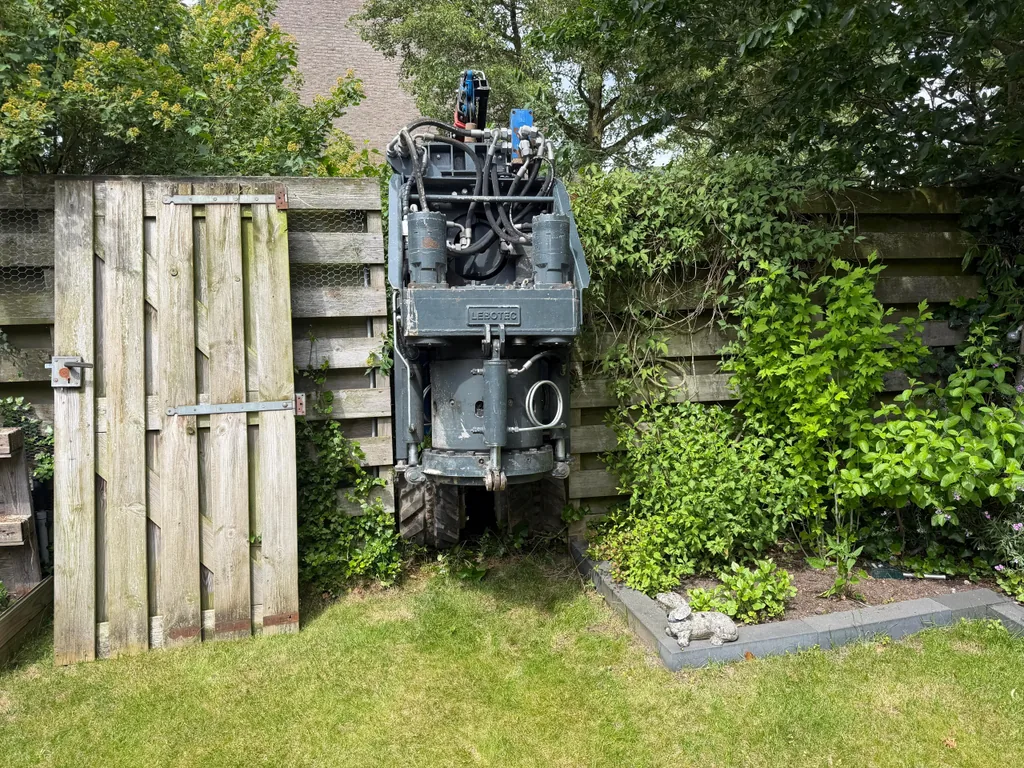 Compacte boormachine CD 45 rijdt door een smalle tuindoorgang naar de werkplek voor casing draaipalen in Roosendaal