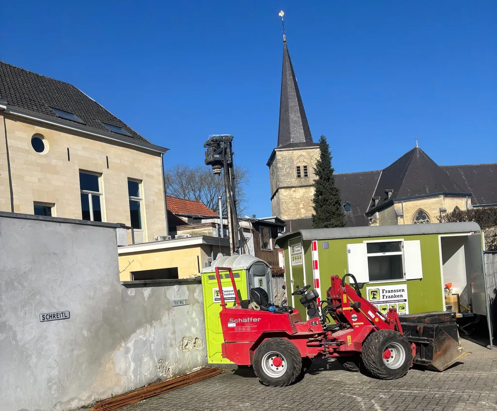 Boormast boven de muur van de werklocatie in Valkenburg, met shovel, bouwkeet en kerktoren