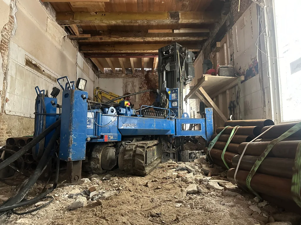 Compacte boorstelling voor schroefinjectiepalen in het gestripte pand aan de Sint Annendwarsstraat in Amsterdam, met gebundelde paalbuizen
