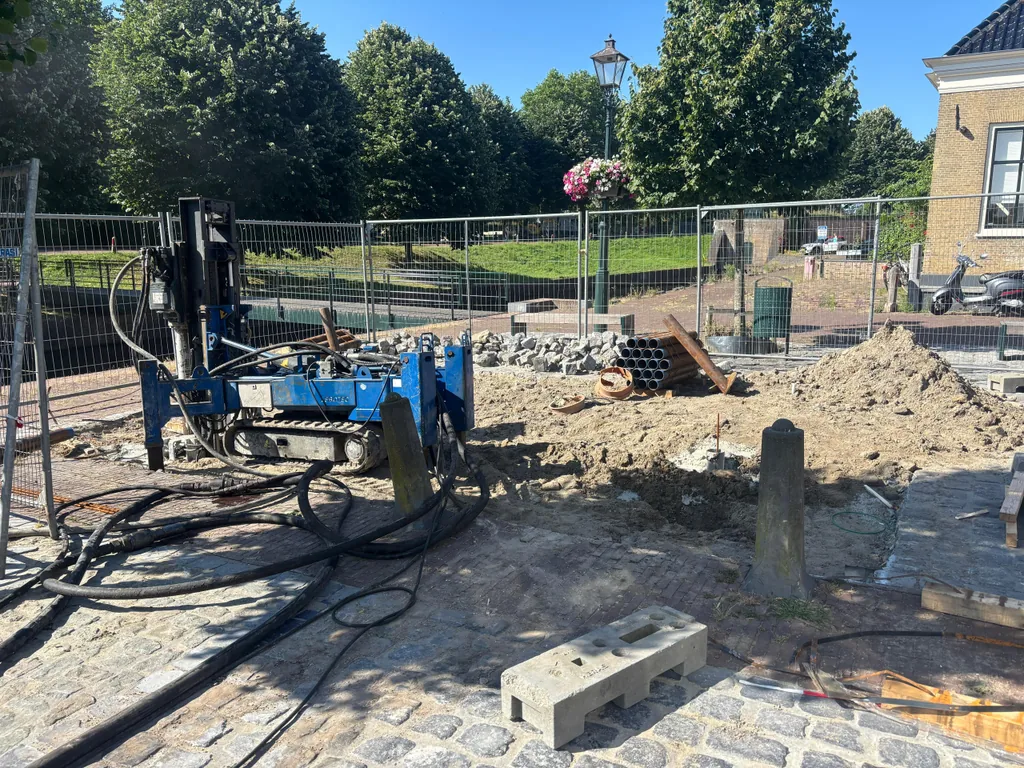 Blauwe boorstelling voor schroefinjectiepalen op een afgezet werkterrein met klinkers en buizen in Brielle