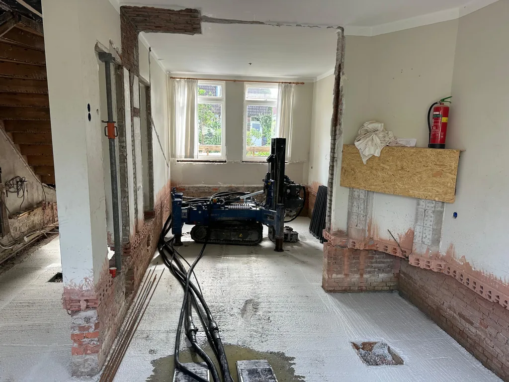 Boorstelling voor schroefinjectiepalen in de gestripte woonkamer van een rijtjeshuis in Duivendrecht, met slangen over de vloer