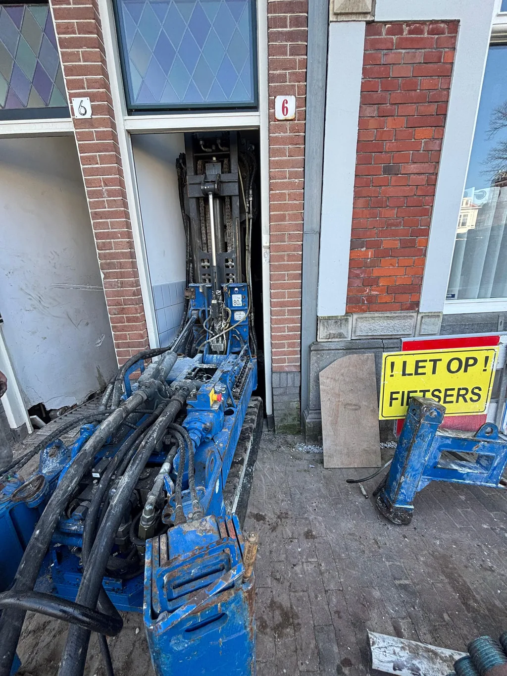 Compacte boorstelling rijdt door de smalle voordeur van een pand aan de Kampersingel in Haarlem voor schroefinjectiepalen