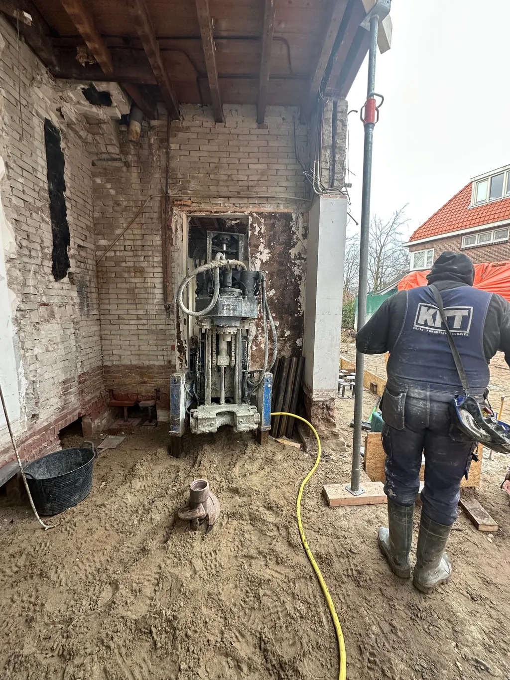 Medewerker van KFT bij een boorstelling die in de opening van de achtergevel schroefinjectiepalen boort in Heemstede