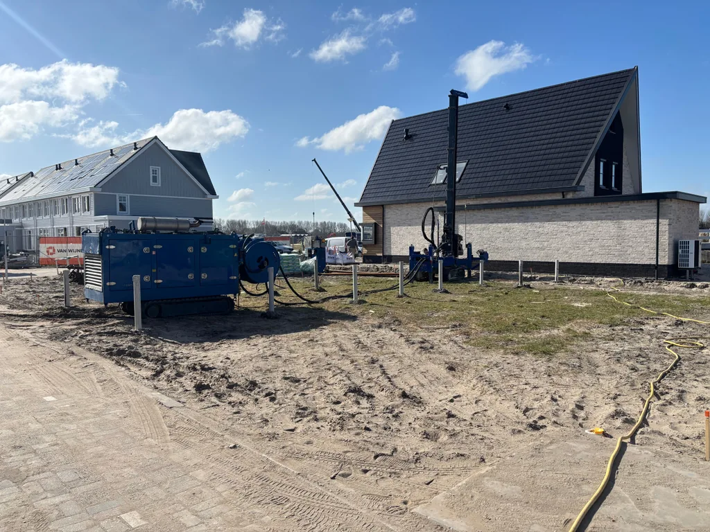 Boorstelling voor schroefinjectiepalen naast een nieuwe woning in Monster, met een blauwe unit en slanghaspel op het terrein