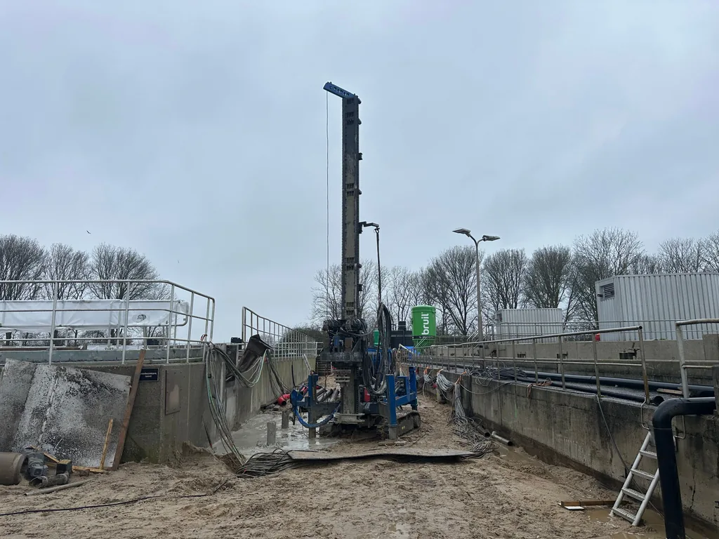 Rechtopstaande boormast voor schroefinjectiepalen tussen de betonnen installaties van waterzuivering RWZI Oijen
