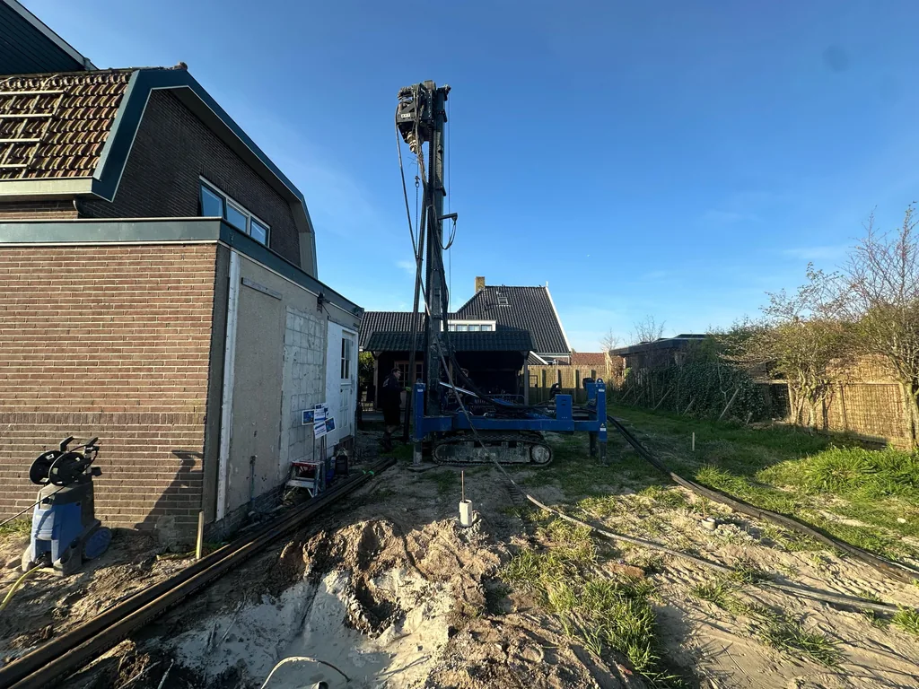 Boorstelling voor schroefinjectiepalen in de tuin naast een woning in Purmerland onder een blauwe lucht