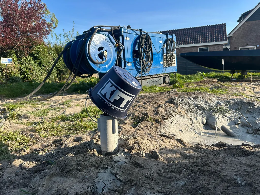 Paalkop van een schroefinjectiepaal met KFT-emmer, met de blauwe unit en slanghaspels erachter in Purmerland