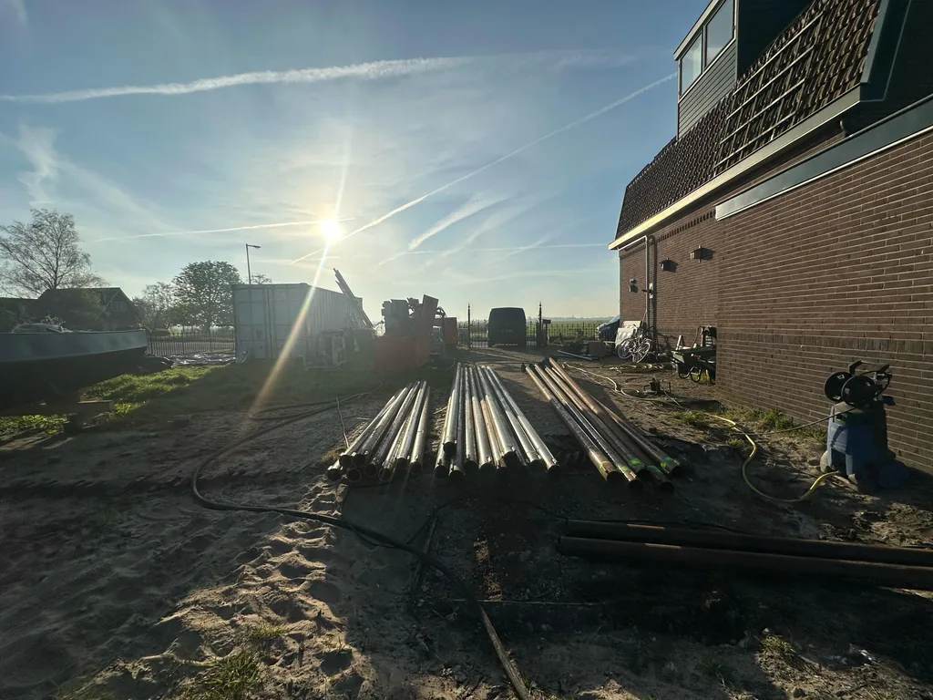 Stalen buizen voor schroefinjectiepalen liggen in stapels op het terrein naast de woning in Purmerland