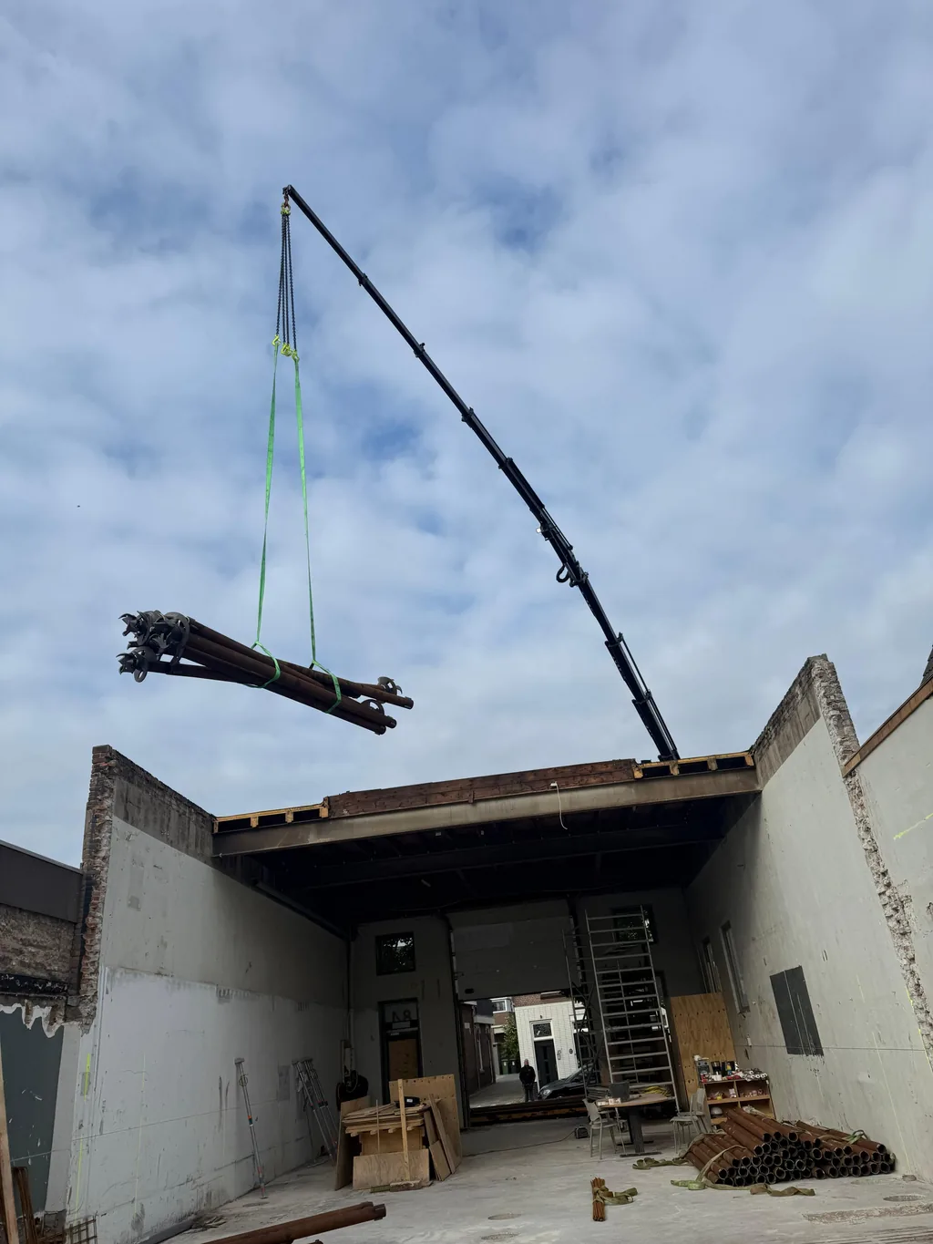 Kraan hijst een bundel paalbuizen voor schroefinjectiepalen over het opengewerkte pand in 's-Gravenzande