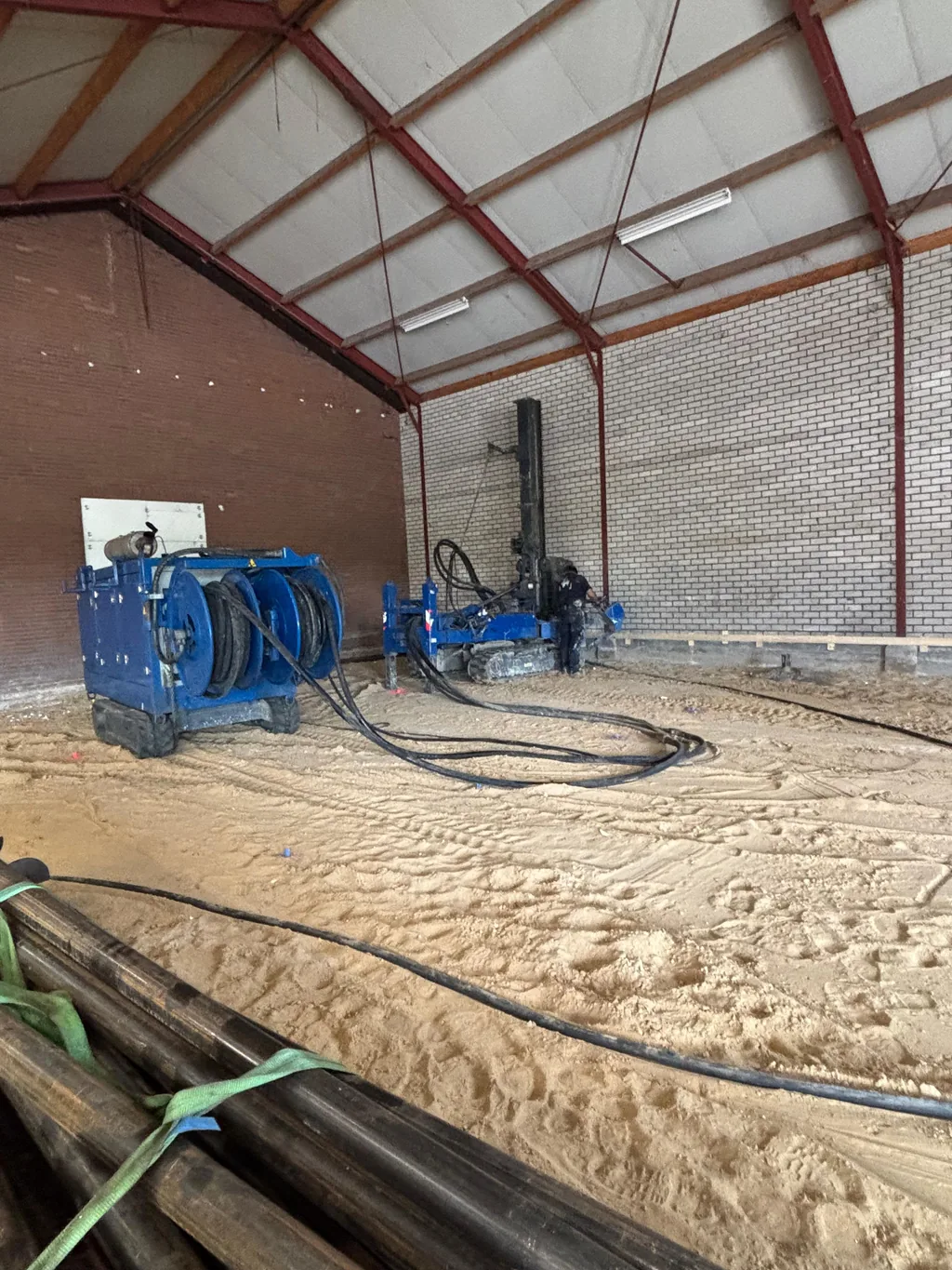 Boorstelling en groutinstallatie voor schroefinjectiepalen in een overdekte loods in Schijndel, met buizen op de voorgrond