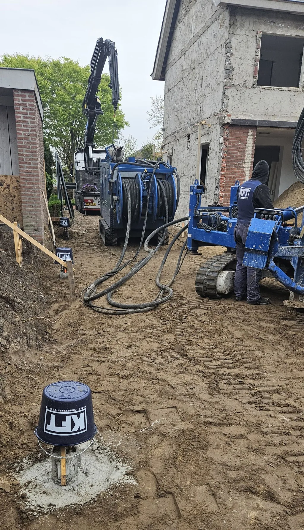 Schroefinjectiepaal met KFT-emmer op de voorgrond, met boorstelling, slanghaspel en kraanwagen naast de woning in Veldhoven
