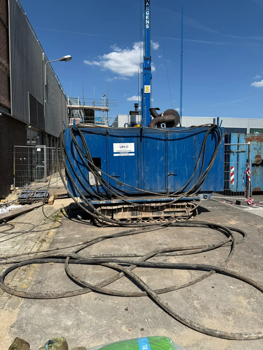 Blauw aggregaat op rupsen met hydraulische slangen op het buitenterrein van het Trefcenter in Venlo tijdens het funderingswerk