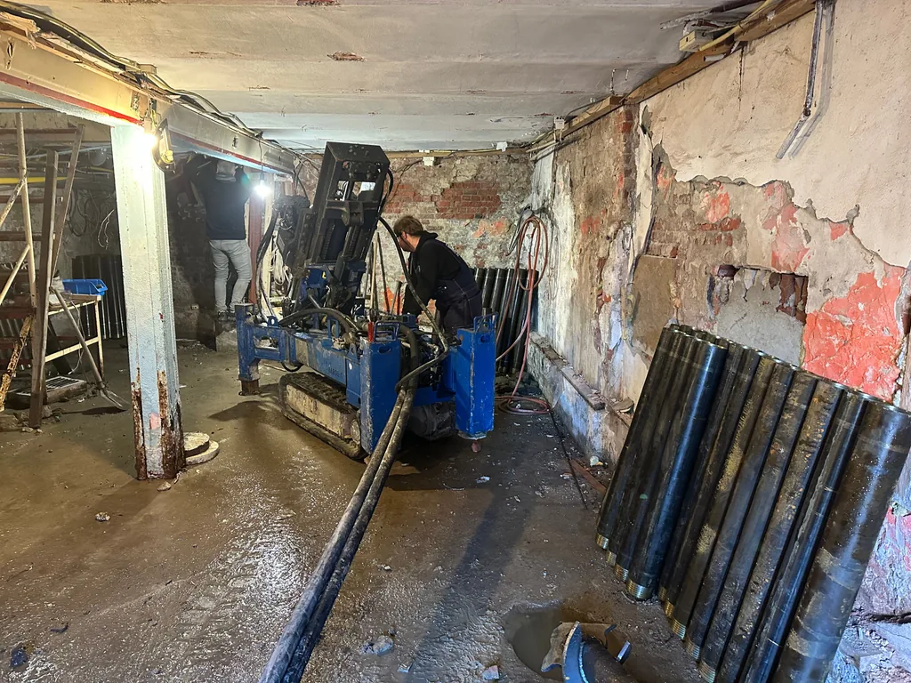 Medewerkers aan het werk met een compacte boorstelling voor schroefinjectiepalen in een lage ruimte van een pand in Zaandam