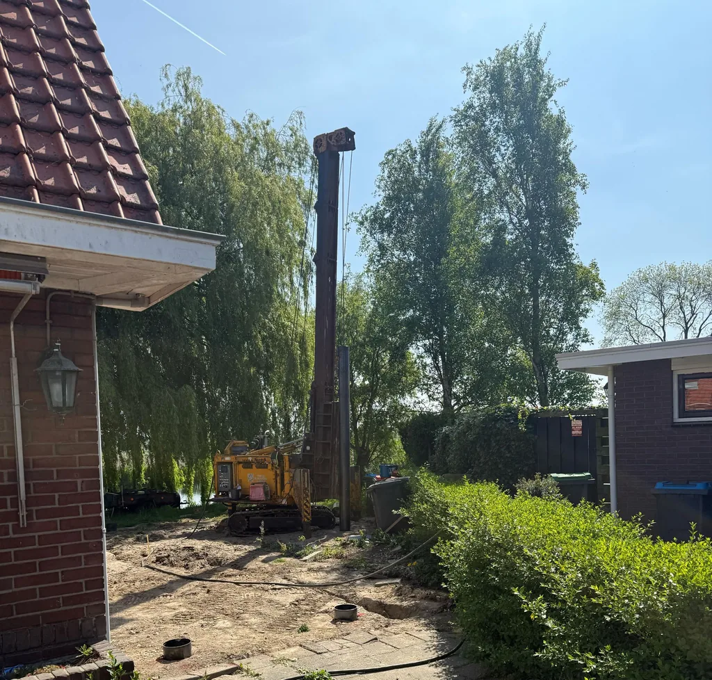 Gele heimachine voor stalen buispalen in de tuin tussen twee woningen in Brielle