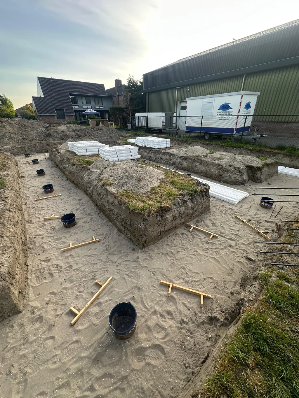 Paalkoppen van geheide stalen buispalen met houten markeringen in een zandige funderingssleuf in Heerhugowaard