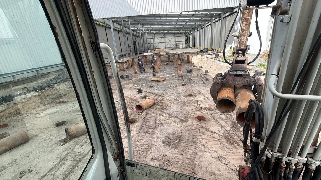 Zicht vanuit de heimachine op stalen buispalen en medewerkers in de magazijnuitbreiding in Lelystad
