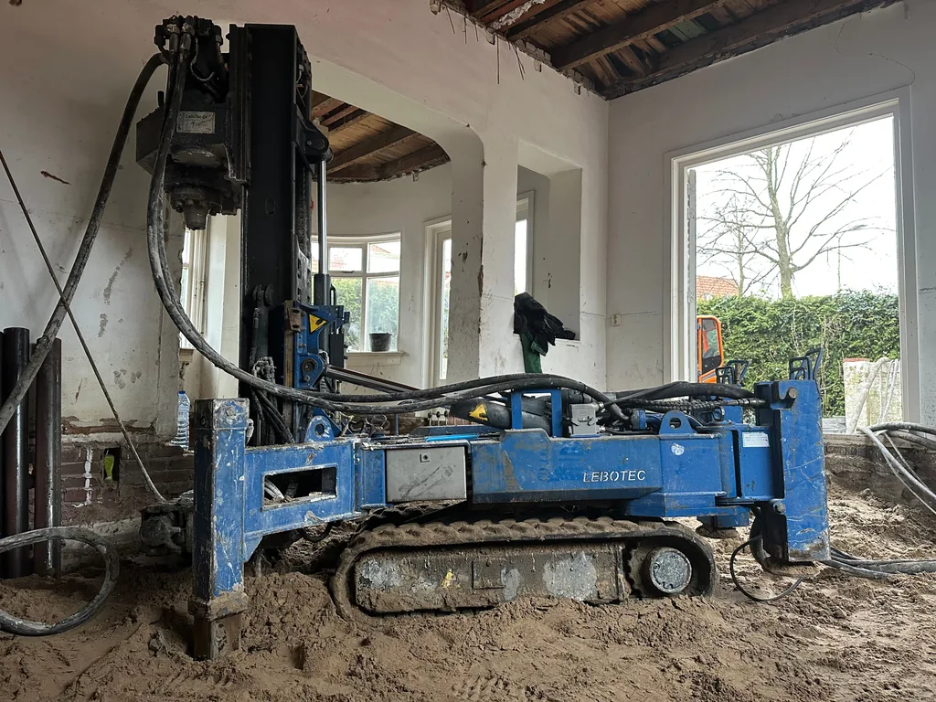 Compacte rupsboorstelling van KFT boort inpandig schroefinjectiepalen in een gestripte woning met erker
