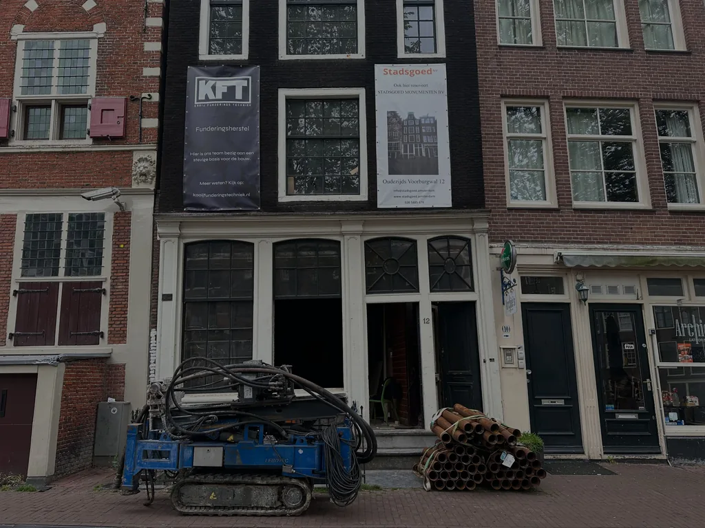 Compacte boorstelling en gestapelde buisdelen voor schroefinjectiepalen (SIP-palen) voor een grachtpand in Amsterdam met KFT-spandoek