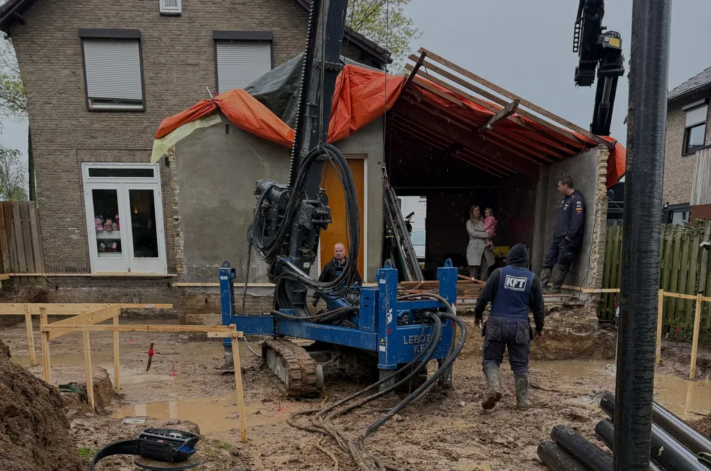 Compacte heistelling brengt stalen buispalen aan voor een uitbouw achter een woning, met buissegmenten op de voorgrond