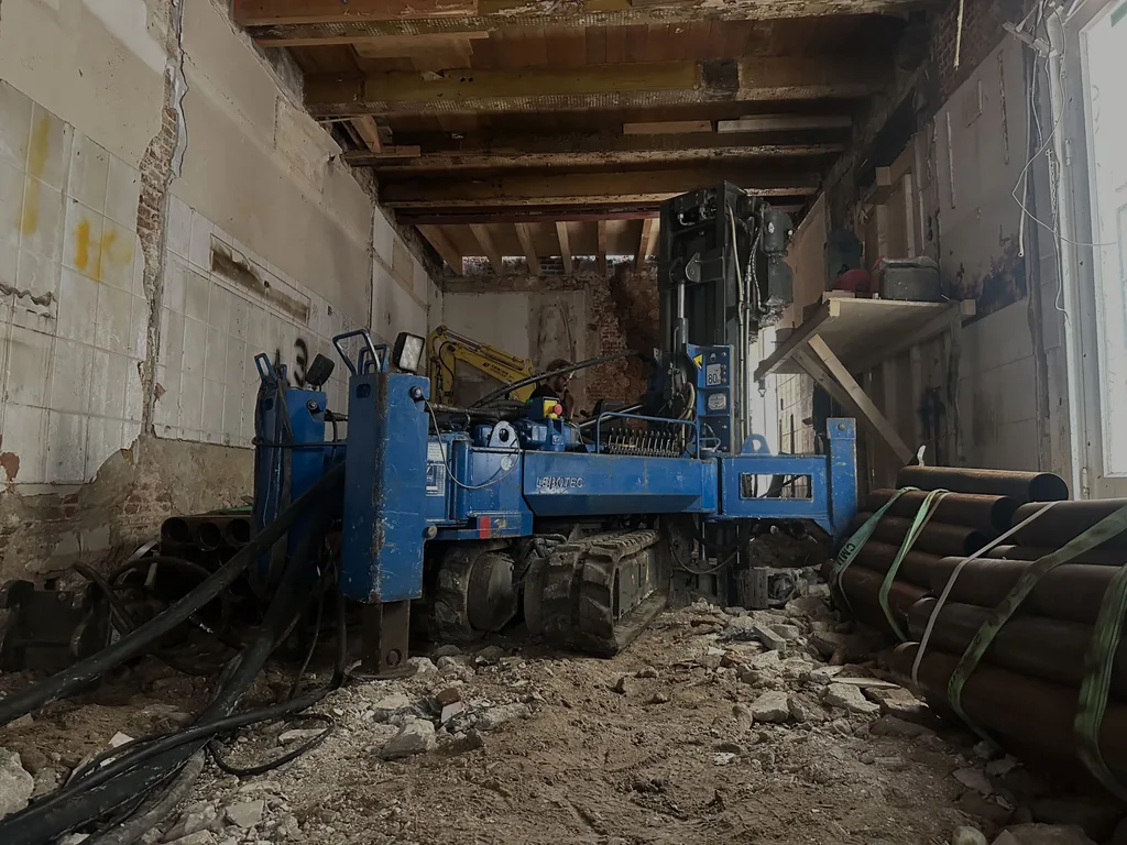 Compacte blauwe boorstelling inpandig in een gestript pand, met gebundelde stalen buizen voor schroefinjectiepalen